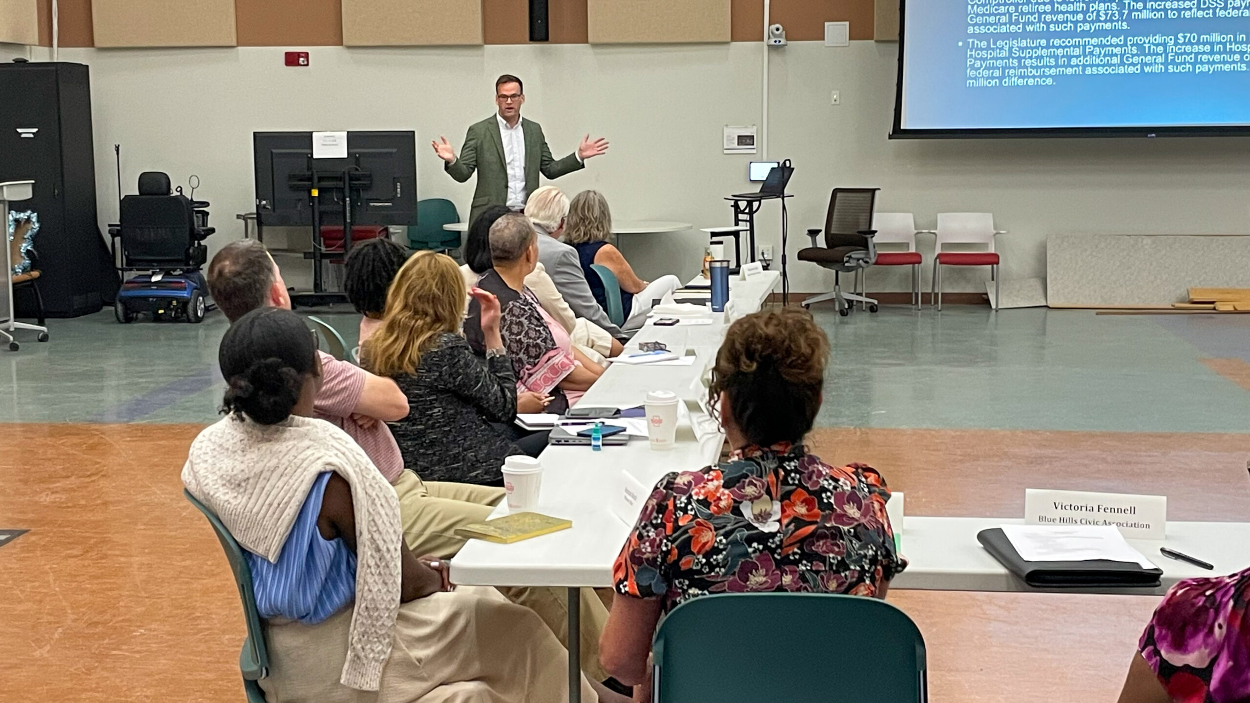 a man presenting at the end of a line of people sitting at tables