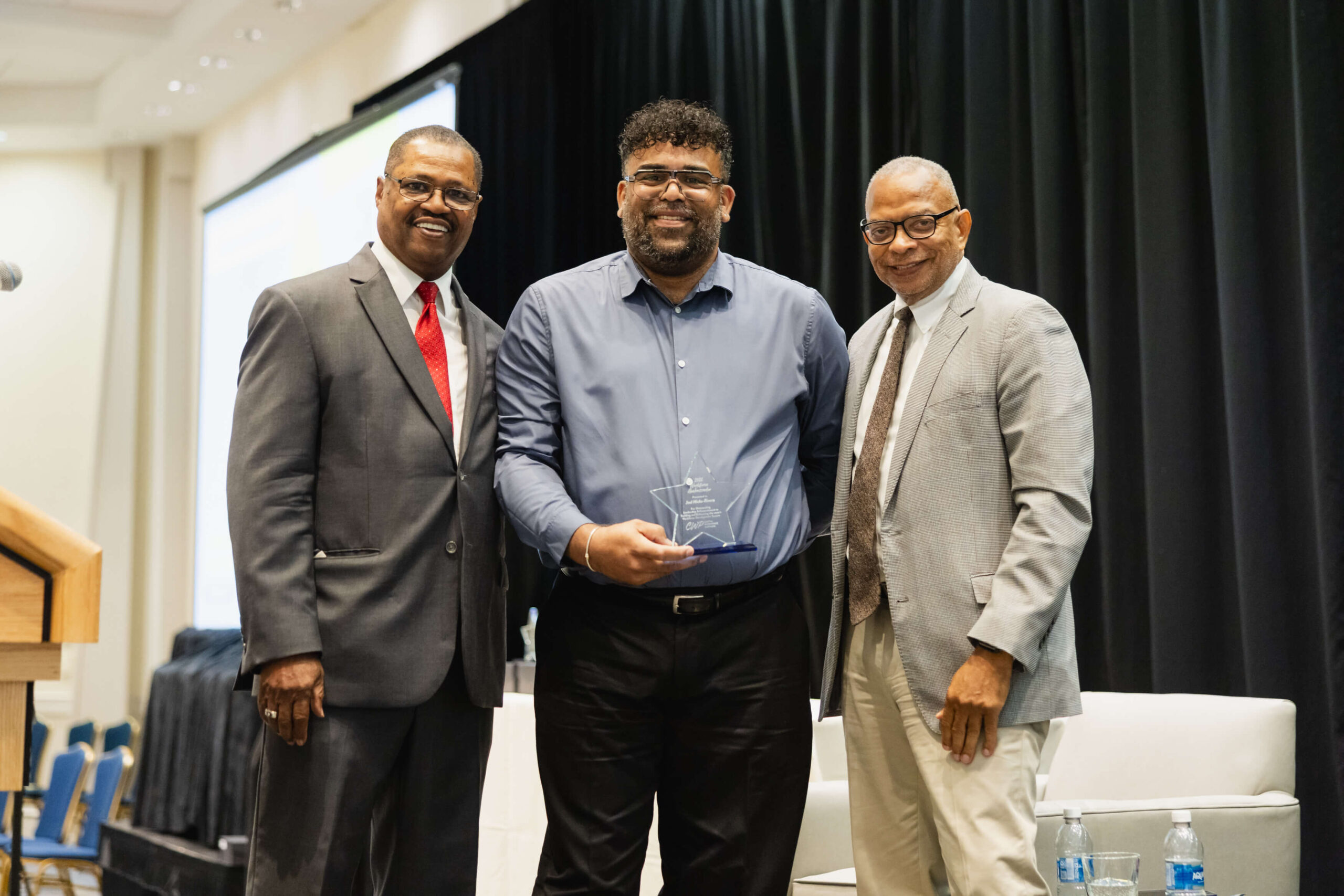 Joel Hicks-Rivera accepting award at CWP 2026 Annual Meeting, with CWP leadership on each side.